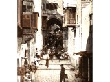 The Street of David runs from Jaffa Gate to the Temple Area of Jerusalem. We see entrances to workshops, stores, shop counters and dove cages hung out. Water carriers take goat-skin containers to fill them at the pipe by the gate.